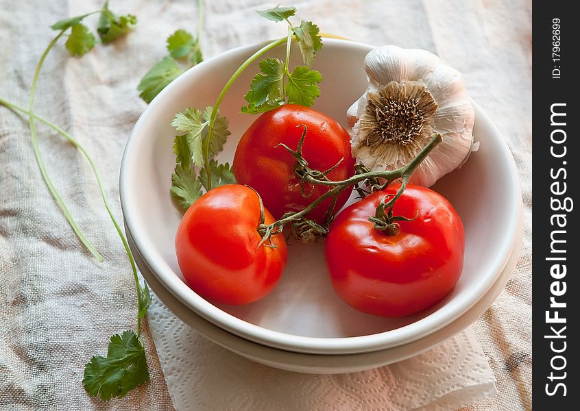 Tomatoes and garlic on a white plate in a rustic setting. Tomatoes and garlic on a white plate in a rustic setting