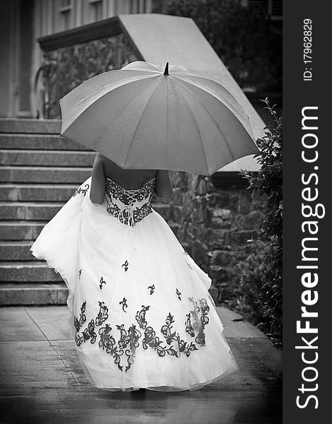 A bride walking away holding an umbrella in black and white. A bride walking away holding an umbrella in black and white