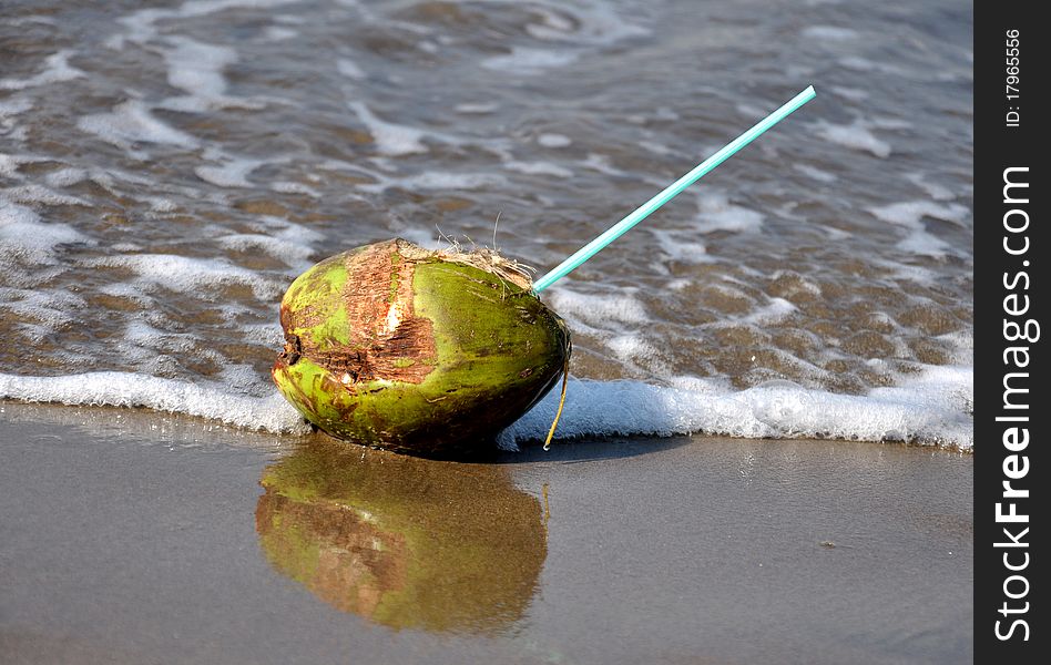 Green coconut with straw at seashore