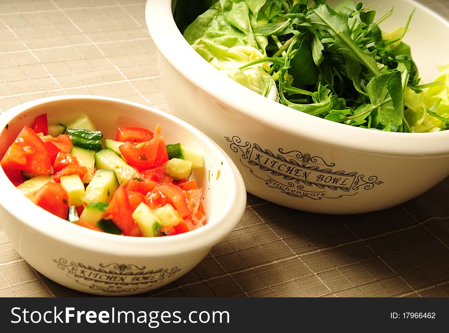Two salad kitchen bowls filled with fresh vegetables on a tablecloth. Two salad kitchen bowls filled with fresh vegetables on a tablecloth