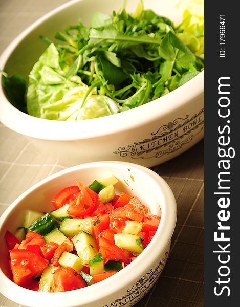 Two salad kitchen bowls filled with fresh vegetables on a tablecloth. Two salad kitchen bowls filled with fresh vegetables on a tablecloth