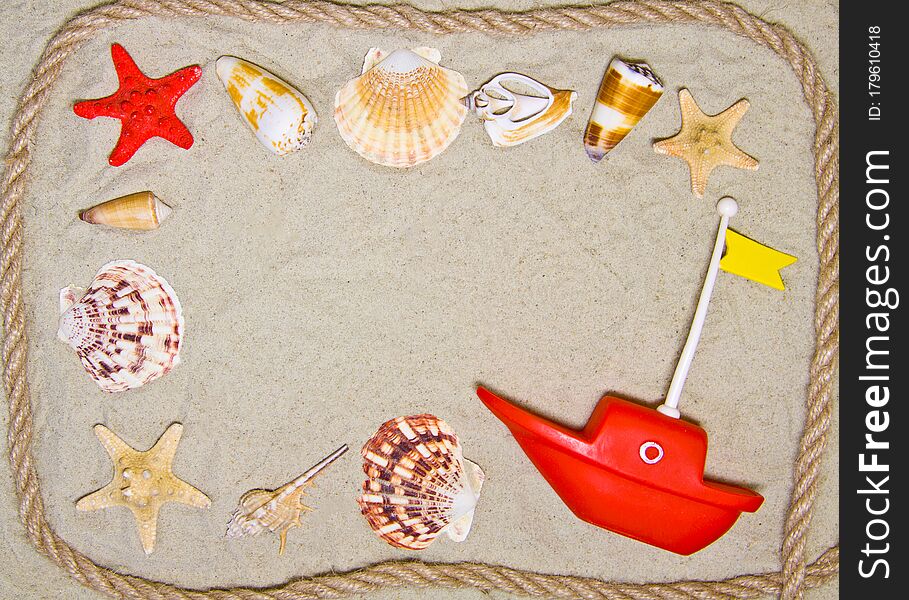 Seashells and nautical rope decoration on sand background with red toy ship.