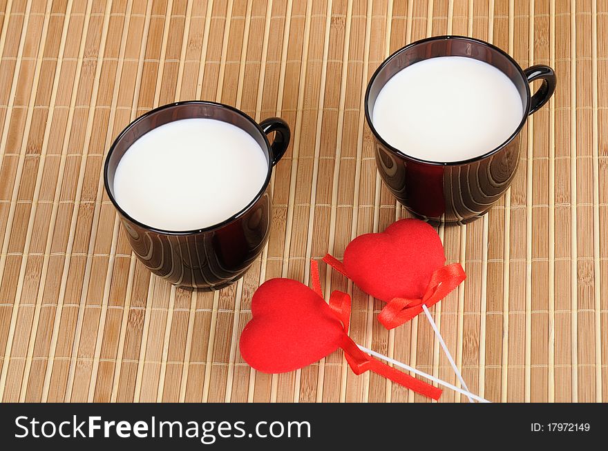 Two cups with milk and red hearts on bamboo background. Two cups with milk and red hearts on bamboo background