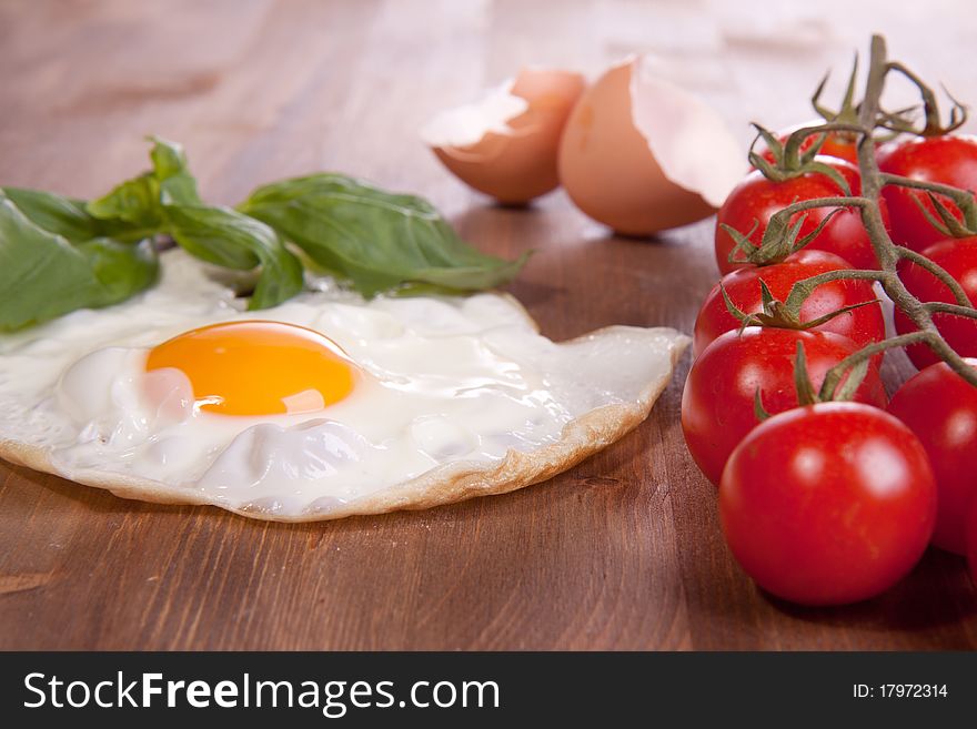 Fried egg served on a wooden table with tomato and fresh herbs. Fried egg served on a wooden table with tomato and fresh herbs