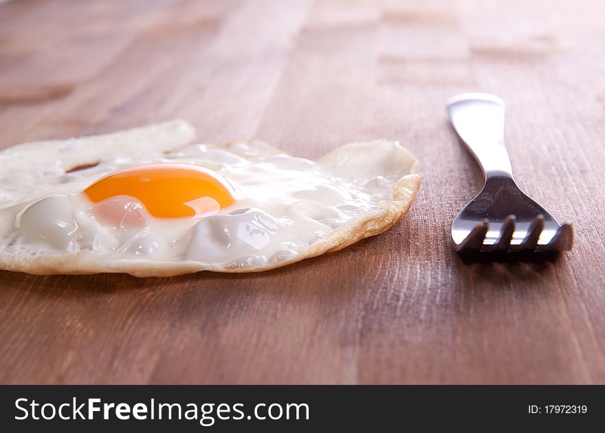 Fried egg served on a wooden table with a metal frog. Fried egg served on a wooden table with a metal frog