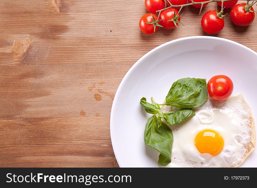 Fried egg served on a wooden table with tomato and fresh herbs. Fried egg served on a wooden table with tomato and fresh herbs
