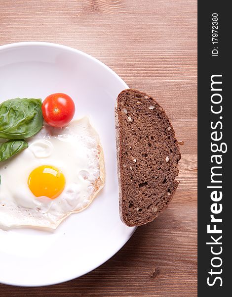 Fried egg served on a wooden table with tomato and fresh herbs. Fried egg served on a wooden table with tomato and fresh herbs