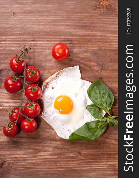 Fried egg served on a wooden table with tomato and fresh herbs. Fried egg served on a wooden table with tomato and fresh herbs