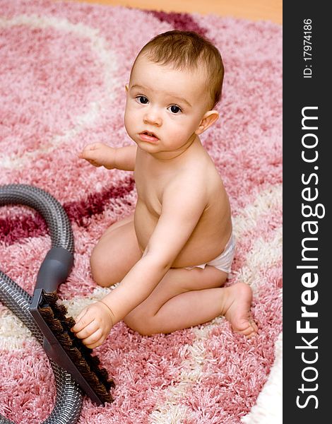 Cute caucasian baby with vacuum cleaner on the carpet