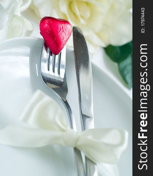 Fork and knife laying on plate with ribbon and heart. Fork and knife laying on plate with ribbon and heart