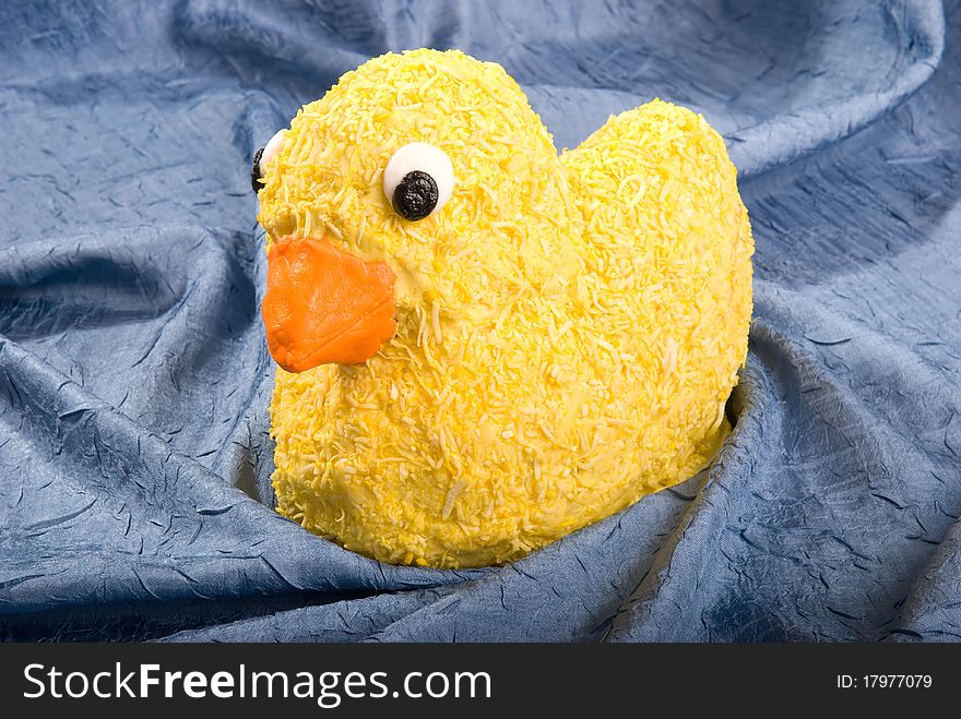 A yellow-coconut covered rubber duck cake sits on a pond of blue fabric.
