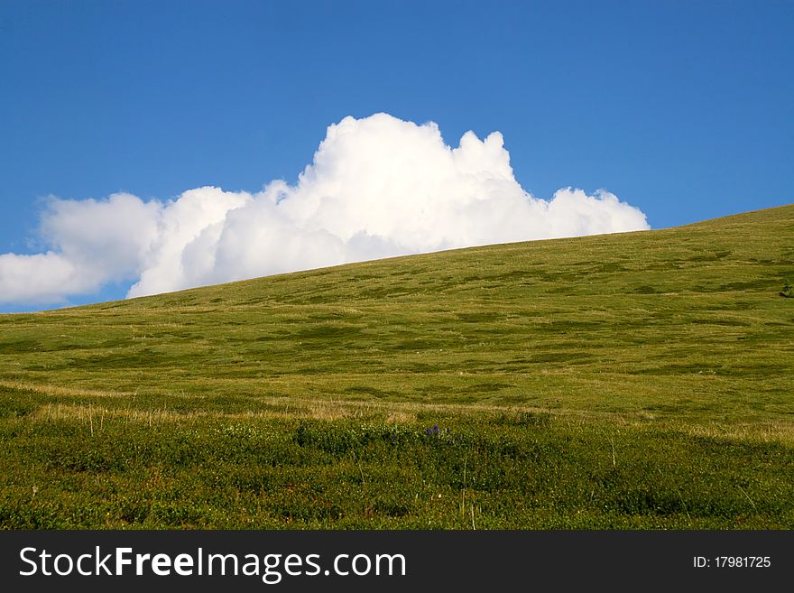 White cloud behind green hill