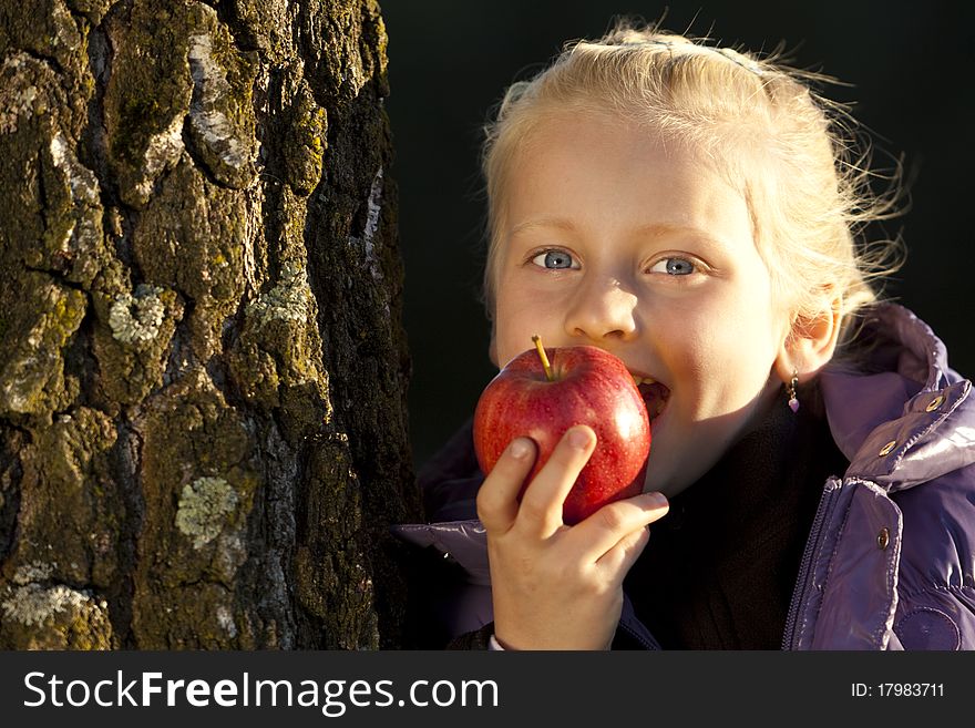 Young girl leans on tree and bite in an appel.