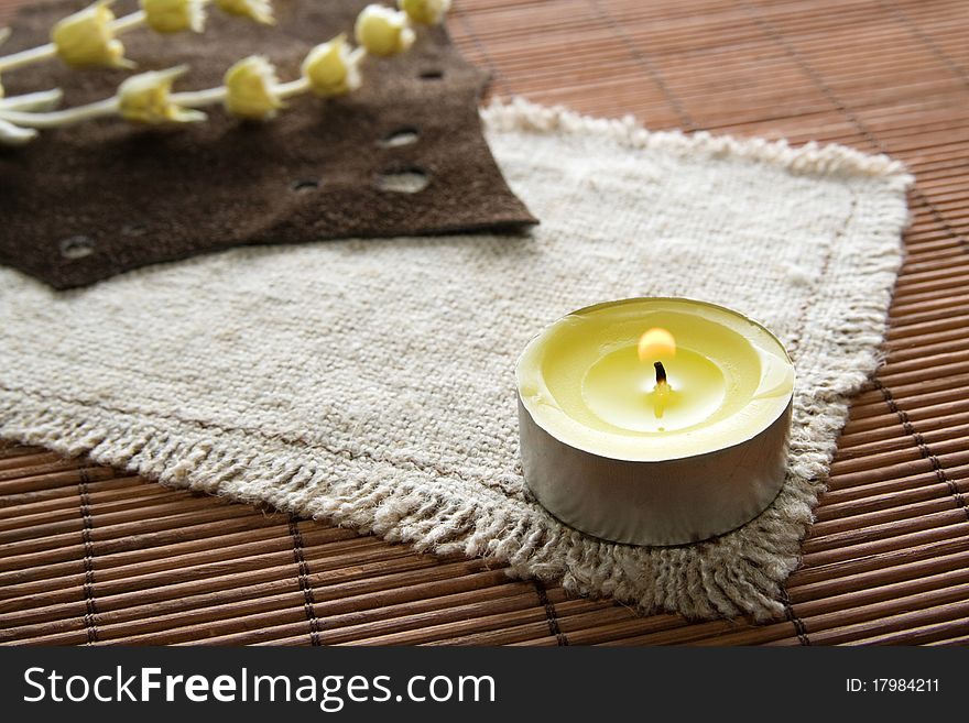 Flaming yellow candle with herbs on textured background. Flaming yellow candle with herbs on textured background