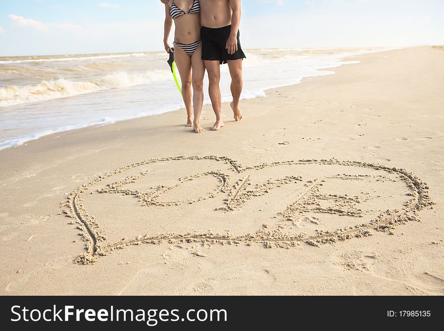 Hearts drawn on the sand of a beach (foreground), the man and woman on the background