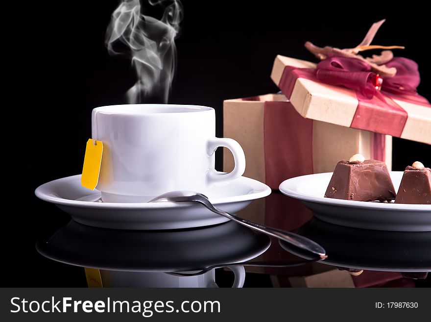 Tea, chocolate and gift on dark background