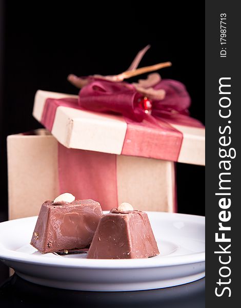 Two chocolate on a plate with gift box on dark background