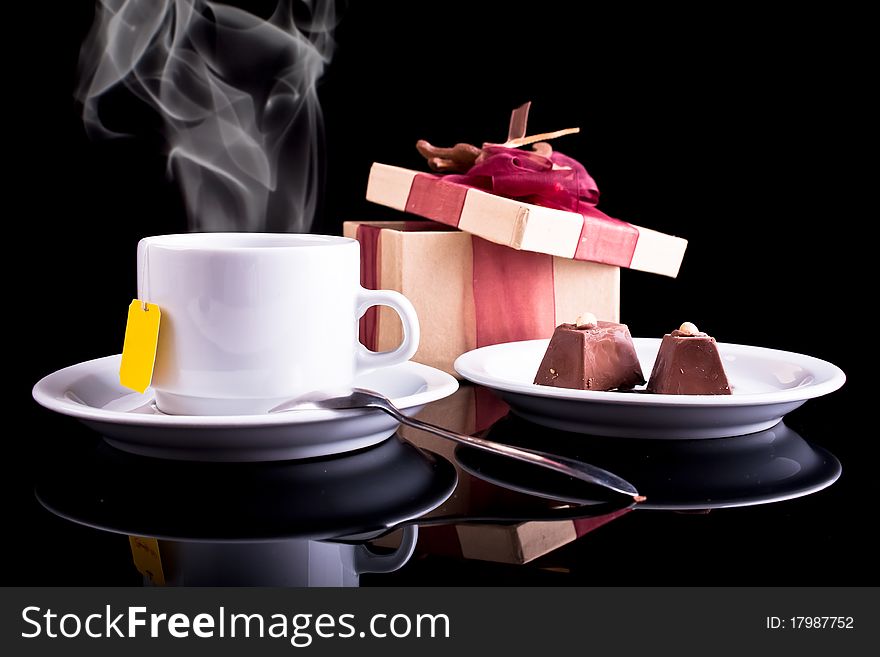 Tea, chocolate and gift on dark background