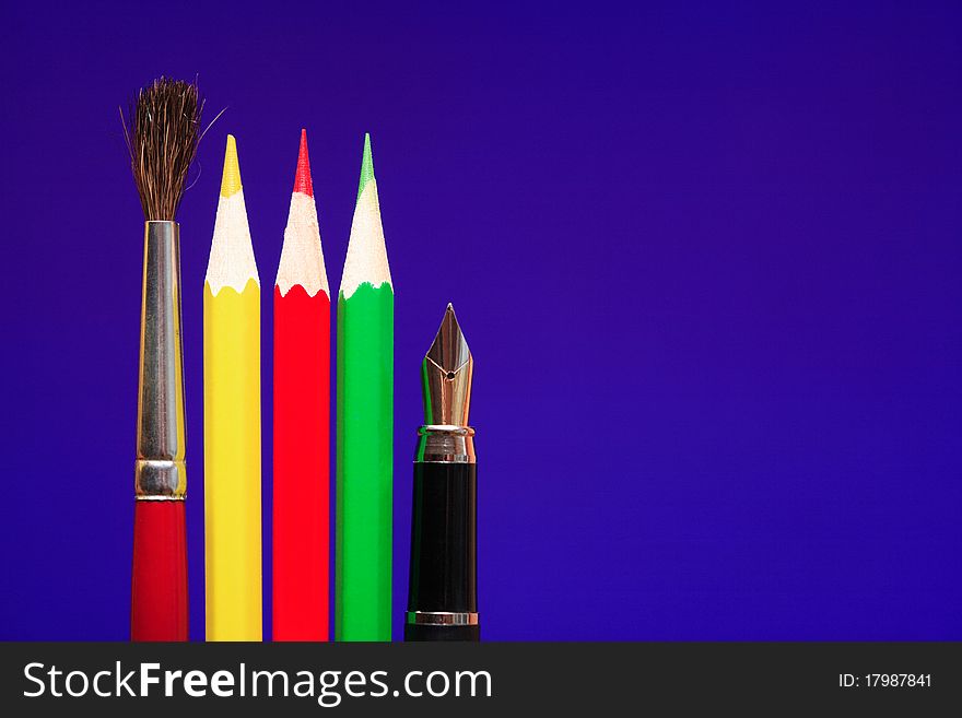 Paintbrush, color pencils and fountain pen standing in a row on blue background. Paintbrush, color pencils and fountain pen standing in a row on blue background