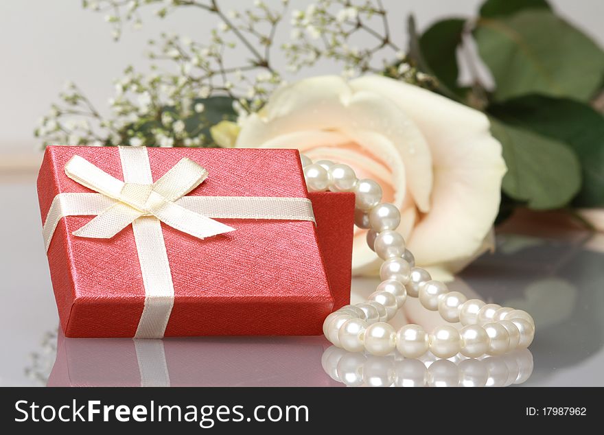 Gift box with pearl necklace near cream rose with reflection. Gift box with pearl necklace near cream rose with reflection