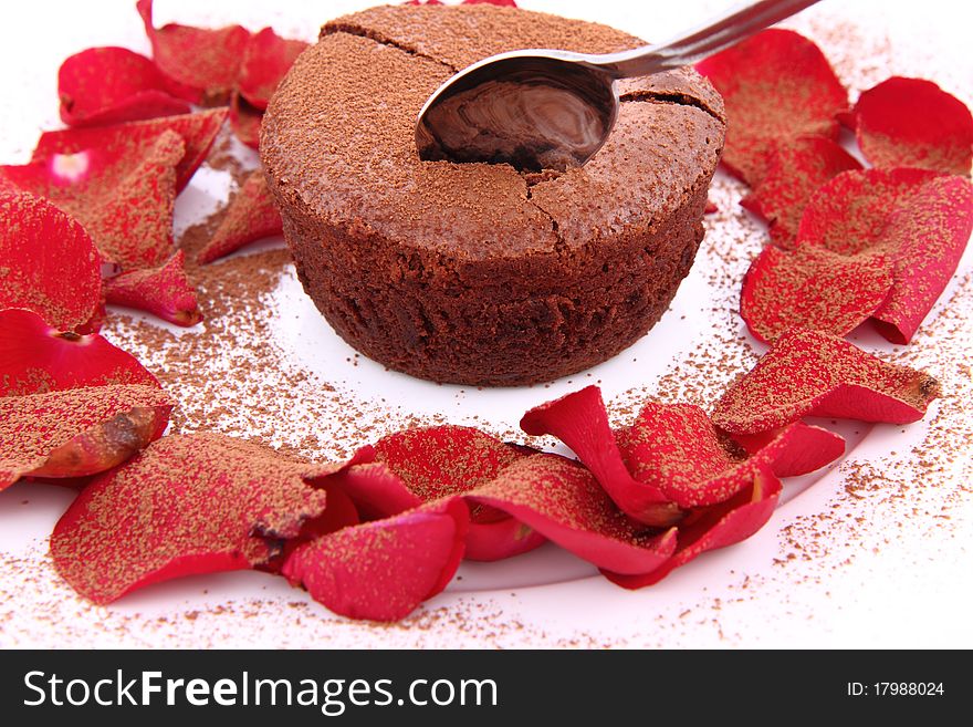 Chocolate souffle decorated with red rose petals and cocoa being eaten with a spoon