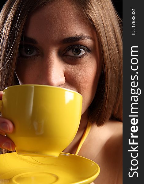 Close up portrait of a beautiful young caucasion woman, drinking tea from a yellow cup and saucer. Close up portrait of a beautiful young caucasion woman, drinking tea from a yellow cup and saucer.