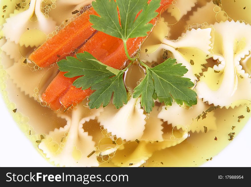 Chicken soup with farfalle pasta and carrots decorated with parsley on a plate