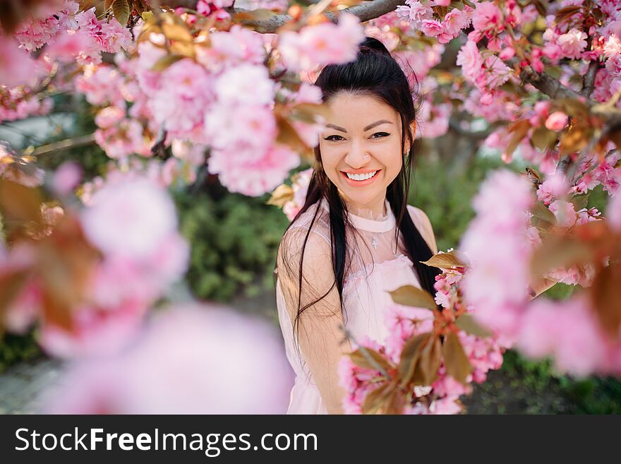 Young woman in white dress has enjoy and relaxes in park with blooming sakura trees. Portrait. Young woman in white dress has enjoy and relaxes in park with blooming sakura trees. Portrait