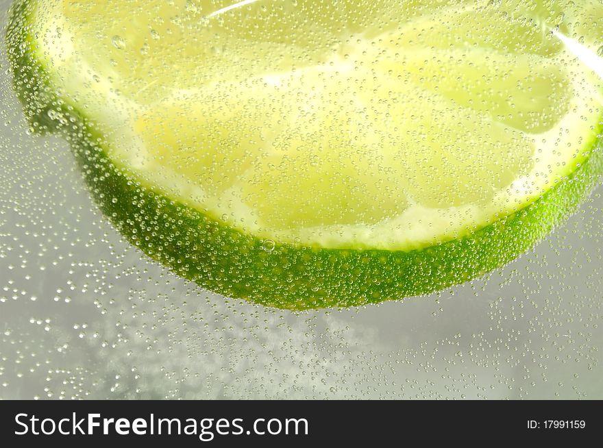 A slice of lime in floating water with bubbles. A slice of lime in floating water with bubbles