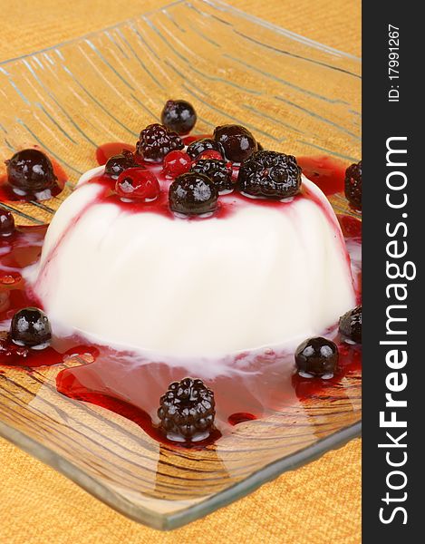 Panna cotta with soft fruits served in glass plate over an orange tablecloth