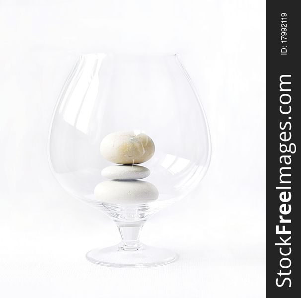 This is photo of big transparent glass with three pebbles on white background. This is photo of big transparent glass with three pebbles on white background.