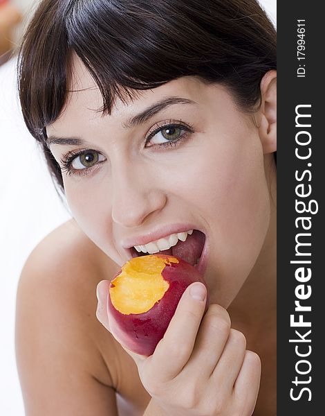 Attractive young woman eating fresh nectarine and smiling. Attractive young woman eating fresh nectarine and smiling