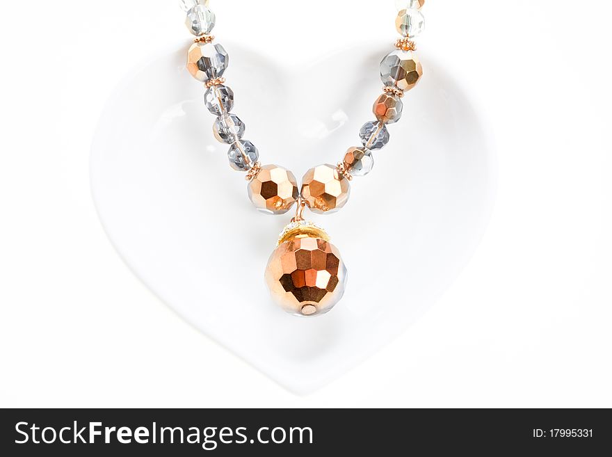 Jewel necklace on heart shaped saucer over white background