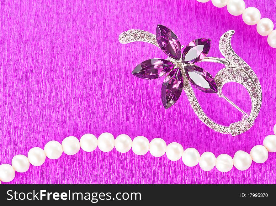 Brooch and pearl necklace on purple background as decorative frame