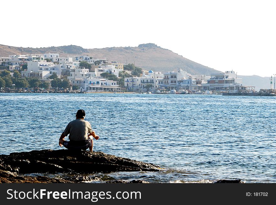 A man fishing in the greek islands with typical architecture in the distance