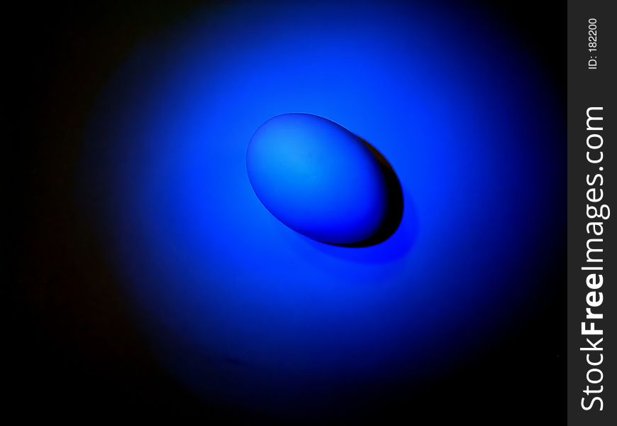 An egg in a blue spotlight on a black background. An egg in a blue spotlight on a black background