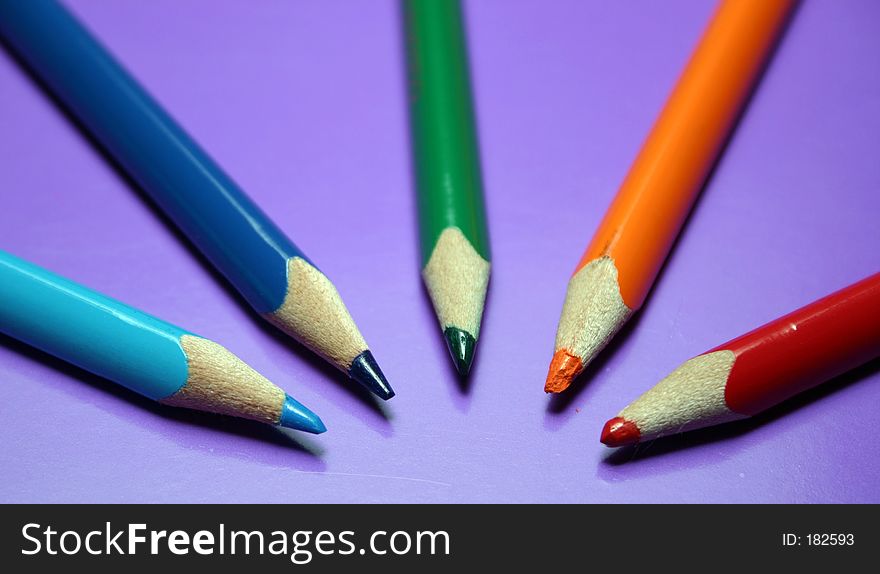 Blue, light blue, orange and red color pencils on a purple background. Blue, light blue, orange and red color pencils on a purple background