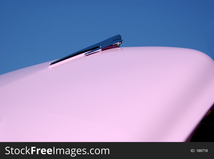 Car ornament on open hood of vintage car pointing to the sky