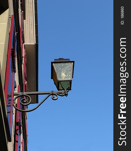 Street light mounted on a house wall on blue sky background. Street light mounted on a house wall on blue sky background