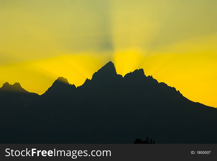 Sunbeams brighten the sky at sunset over the silhouetted mountains in Grand Teton National Park. Sunbeams brighten the sky at sunset over the silhouetted mountains in Grand Teton National Park