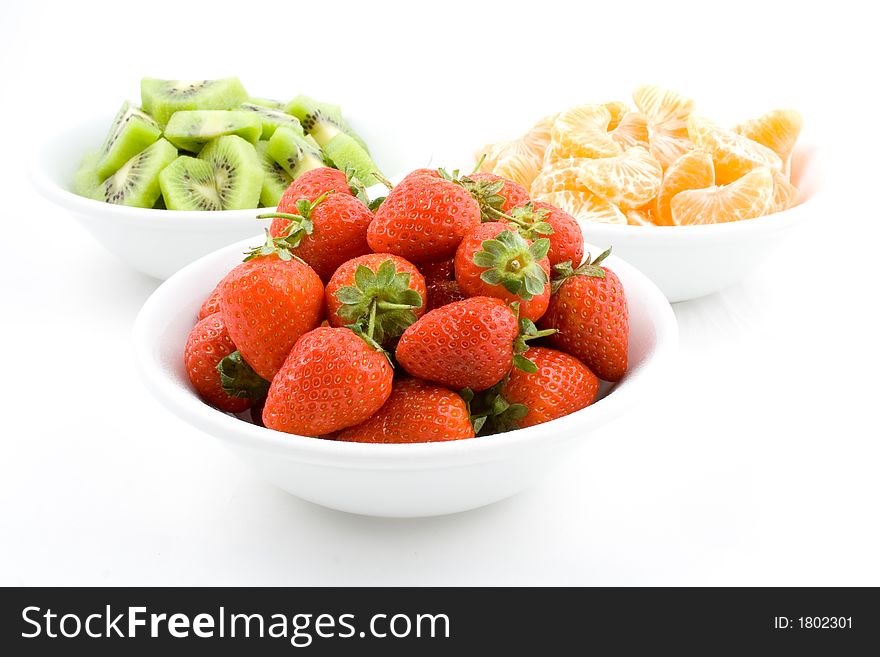Kiwi, strawberries and mandarines on white bowls, white background, isolated. Kiwi, strawberries and mandarines on white bowls, white background, isolated.