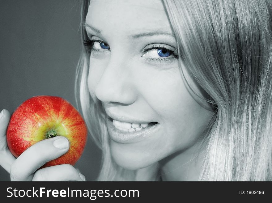 A smiling young blond woman is holding a apple in her hand. A smiling young blond woman is holding a apple in her hand