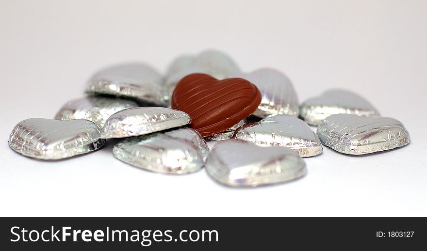 A  chocolate heart is in a sea of silver hearts. A  chocolate heart is in a sea of silver hearts.