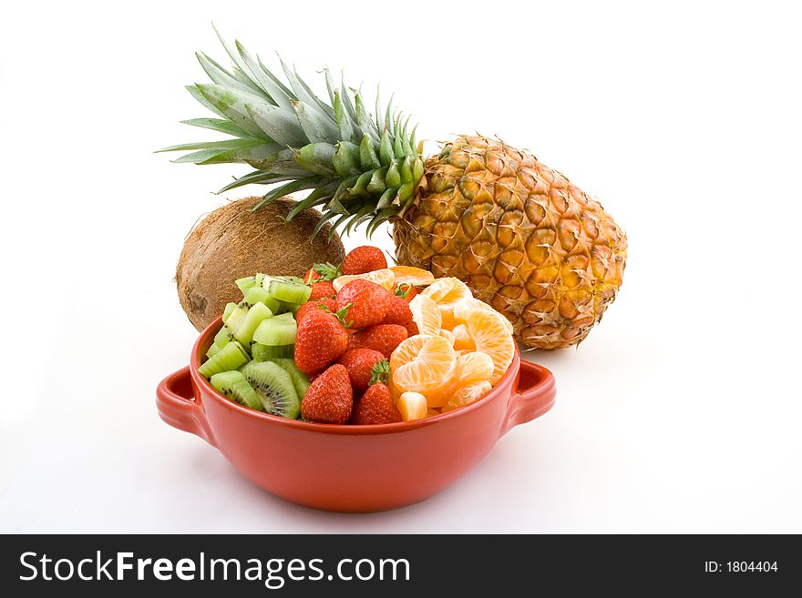 Some fruit mixture, strawberries kiwi and tangerine in red bowl with pineapple and coconut in the background. Some fruit mixture, strawberries kiwi and tangerine in red bowl with pineapple and coconut in the background.