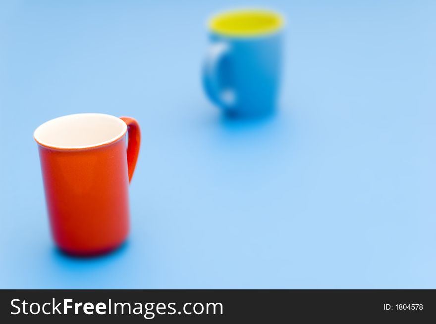 Abstract of red cup with interior white, and blue cup with interior yellow, taken on a light blue background. Red cup in front is in focus; blue cup in back is not. Abstract of red cup with interior white, and blue cup with interior yellow, taken on a light blue background. Red cup in front is in focus; blue cup in back is not.