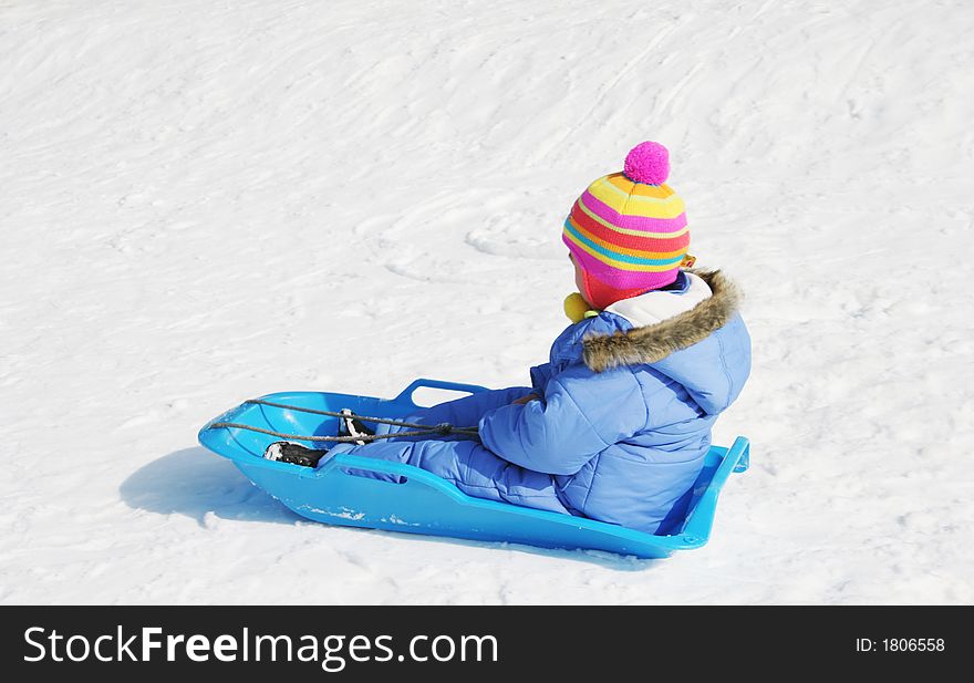 Youngster wearing colorful ski clothing rides a sled. Youngster wearing colorful ski clothing rides a sled