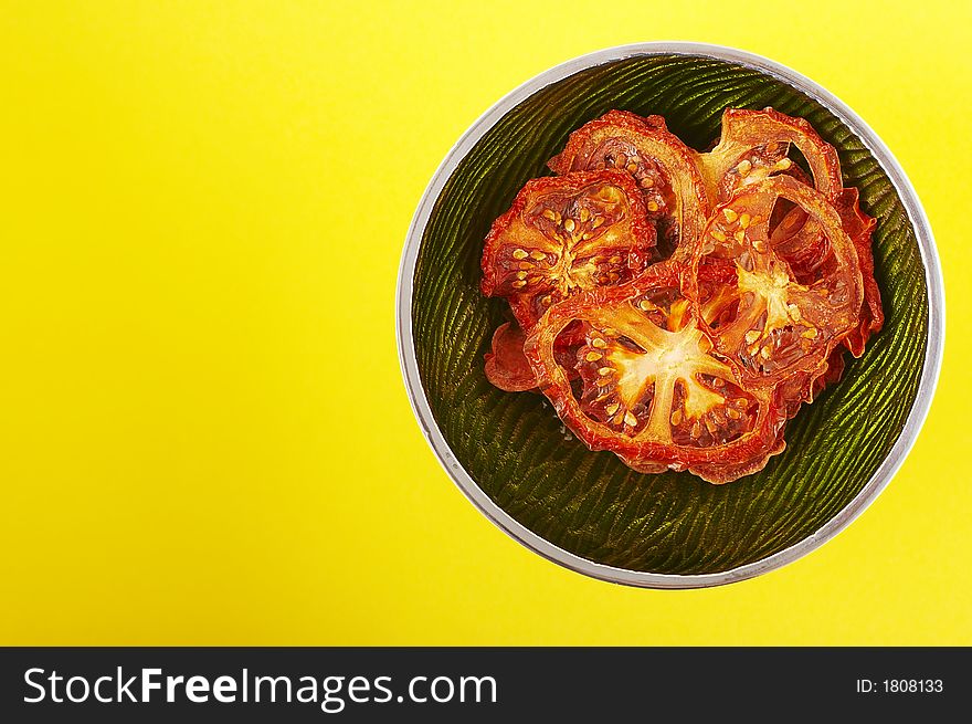 Dried sliced tomatoes in green bowl on the yellow background. Dried sliced tomatoes in green bowl on the yellow background.