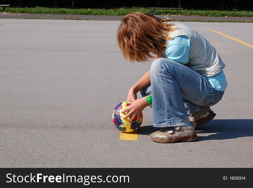 Teenage girl on a playground, crouching and playing with the ball. Teenage girl on a playground, crouching and playing with the ball.