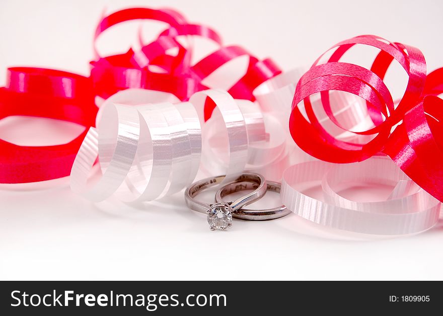 Red and white ribbons on a white background with a set of wedding rings. Red and white ribbons on a white background with a set of wedding rings