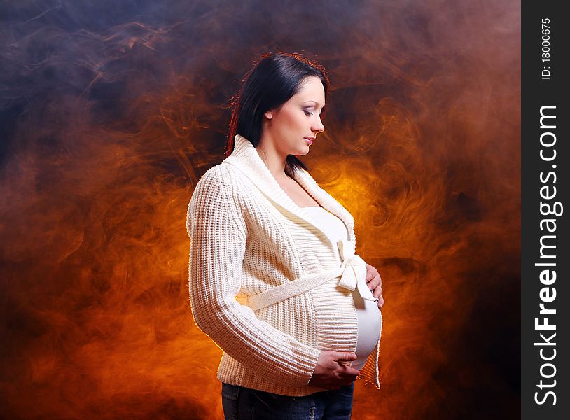 Young and beautiful pregnant woman on black background with smoke